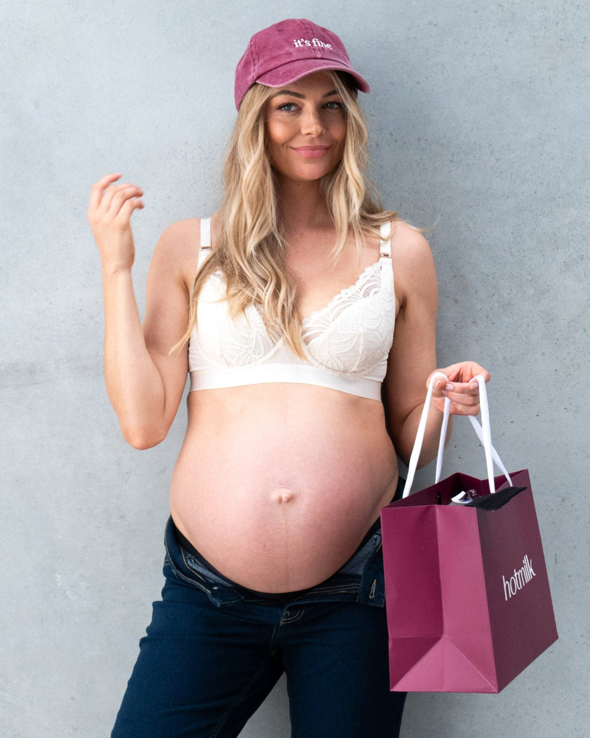 Pregnant woman wearing burgundy "it's fine" cap with Hotmilk Lingerie shopping bag